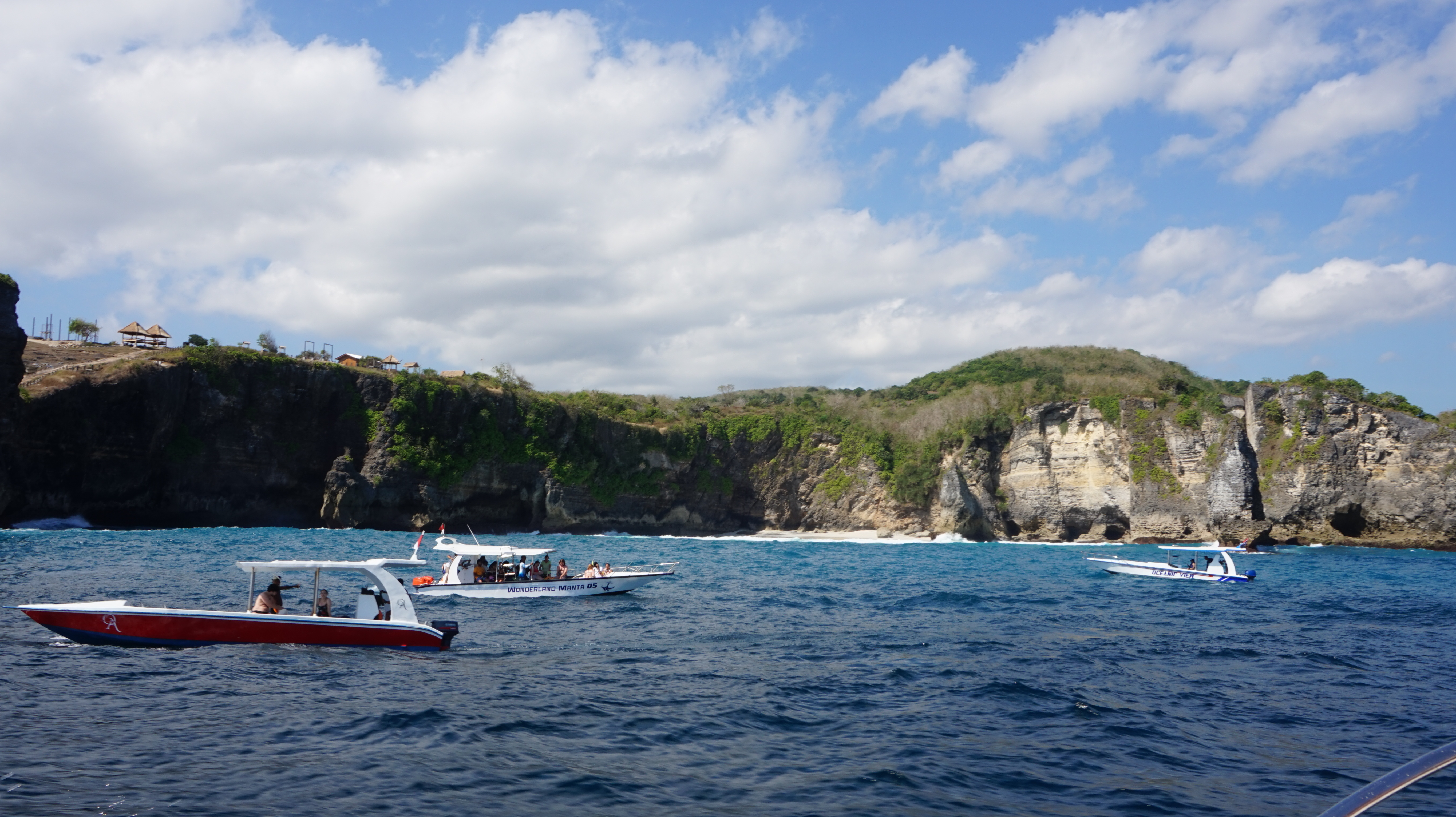 A big rocky cliff and several boats in front of it